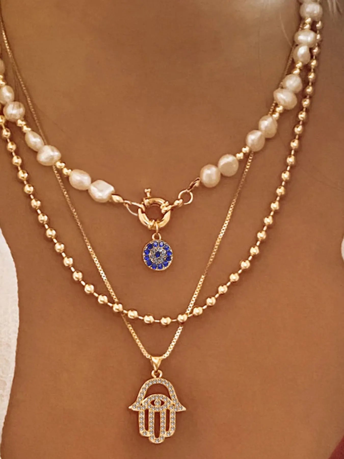 Layered pearl chain necklace with gold-plated evil eye and hamsa pendants on model's neck