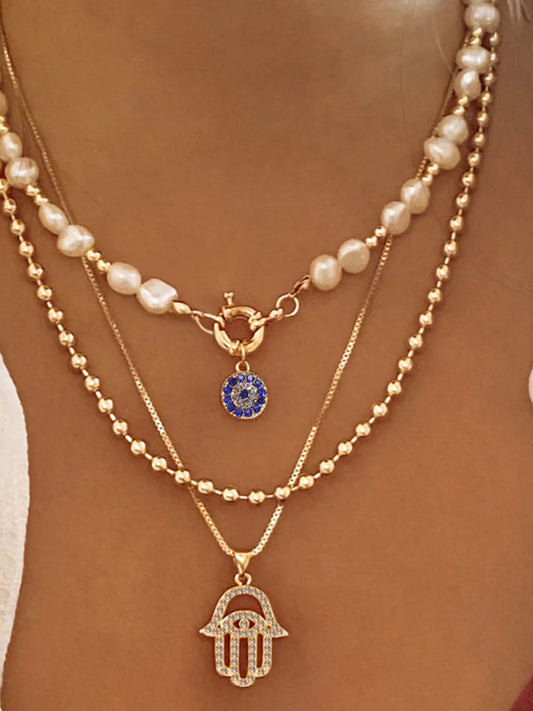 Layered pearl chain necklace with gold-plated evil eye and hamsa pendants on model's neck
